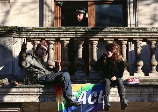 December 24, 2014: A police officer looks on from a doorway as squatters from a group calling themselves 'Love Activists' sit on the balcony of a previously unoccupied building in Trafalgar Square (Photo by Carl Court/Getty Images)